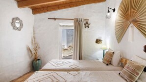 A bedroom with a wooden ceiling, a bed with patterned bedding, a nightstand with a lamp, and a view of the beach through a window. - Country House 'Quinta Do Silêncio T2' with Mountain View, Wi-Fi and Air Conditioning (Tavira)