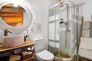 Une salle de bain avec un miroir rond, un lavabo, des toilettes et une douche à parois de verre.