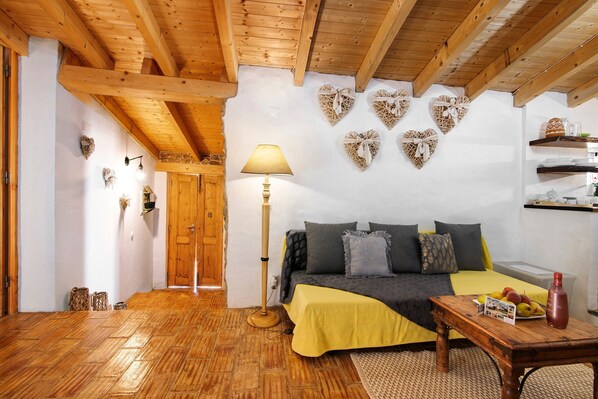 Una habitación acogedora con techo de madera, una cama con manta amarilla, una mesita de noche con una botella roja y adornos decorativos con forma de corazón en las paredes.