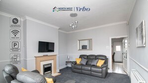 A modern living room with a fireplace, leather sofas, and a flat-screen TV. - Bolton 2 Bedroom House | Free Parking & WiFi | Ideal for Long Stays (Tonge Fold)