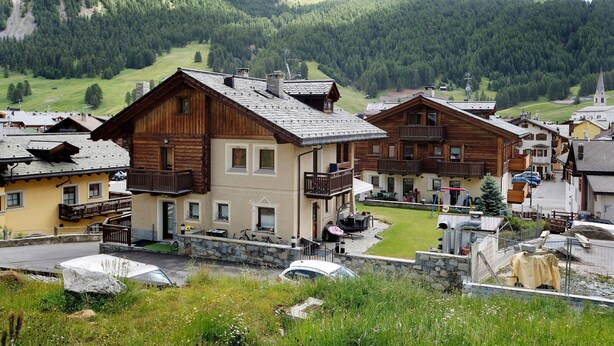 A mountain village with wooden houses, a church, and a ski lift in the background.