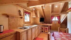 A wooden interior with a kitchen area, wooden cabinets, a dining table, and a red rug.