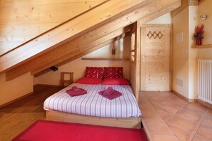 A bedroom with a sloped ceiling, wooden bed frame, red bedding, and a small bedside table.