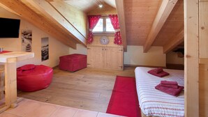 A wooden attic bedroom with a bed, a red bean bag, a small table, and a window with curtains.