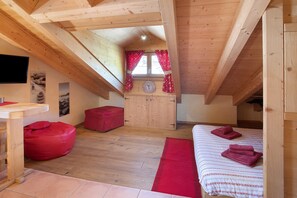 A wooden attic bedroom with a bed, a red bean bag, a small table, and a window with curtains.