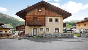 A two-story wooden building with balconies, a stone wall, and a mountain backdrop.