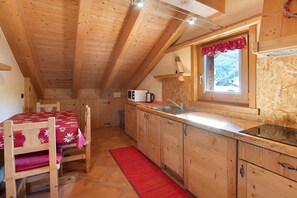 A wooden interior with a kitchen area, including a table with chairs, a microwave, and a window with a view.