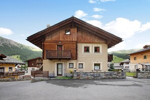 A two-story wooden building with balconies, a stone wall, and a mountain backdrop.