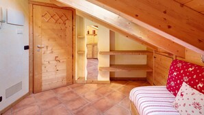 Une pièce en bois avec un plafond en pente, un lit recouvert d’une literie à motifs, un oreiller rouge et une porte en bois.