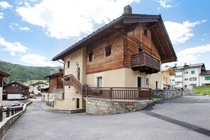 Un edificio de madera tradicional con balcón, base de piedra y una calle empedrada.