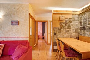 A cozy room with a wooden dining table, red upholstered sofa, and a stone wall.