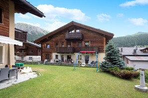 A wooden chalet with a balcony, a swing set, and a well-maintained lawn.
