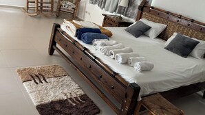 A well-lit bedroom with a large bed, a wooden rocking chair, a small table, and a ceiling fan.