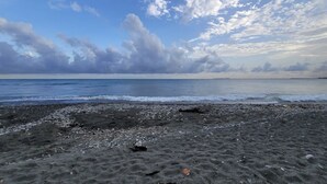 A beach with pebbles and a view of the ocean under a partly cloudy sky.
