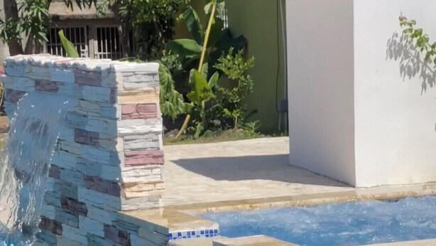 A swimming pool with a stone waterfall feature and a wicker lounge chair.