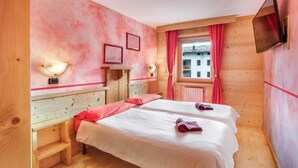 Ein Zimmer mit zwei Betten, Holzwänden, einem Fenster mit roten Vorhängen und einem an der Wand befestigten Fernseher.