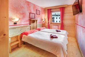 A room with two beds, wooden walls, a window with red curtains, and a mounted TV.