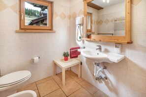 A bathroom with a toilet, sink, mirror, and a small table with a plant.