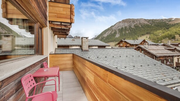Ein Holzbalkon mit Tisch und Stühlen mit Blick auf eine gebirgige Landschaft.