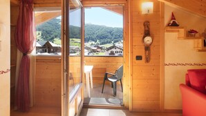 Een houten interieur met een balkon, een stoel, een tafel, een rode bank en een klok aan de muur.