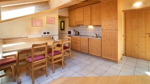 Een houten keuken met een eettafel en stoelen, houten kasten en een betegelde vloer.