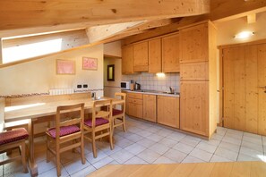 A wooden kitchen with a dining table and chairs, wooden cabinets, and a tiled floor.