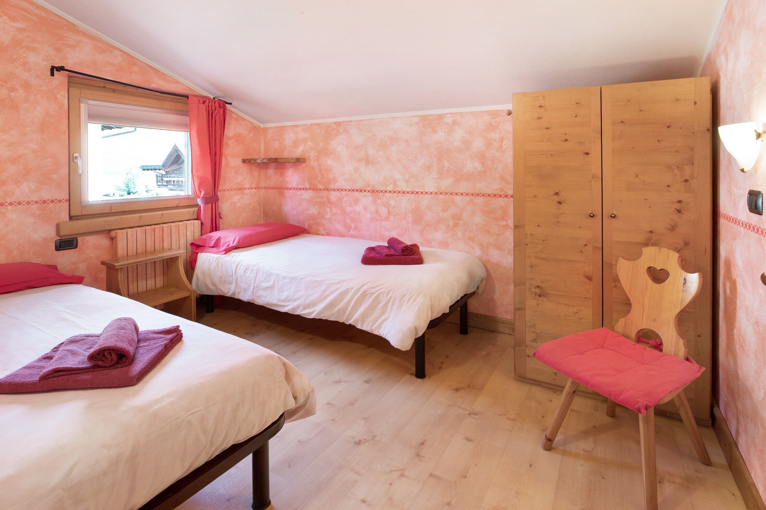 Une chambre avec deux lits, une armoire en bois, une fenêtre donnant sur un beau paysage et une chaise en bois.