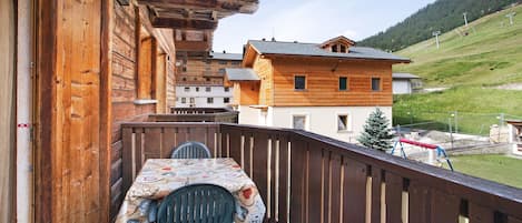 A wooden balcony with a table and chairs, overlooking a hillside with buildings and a ski lift.