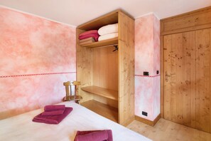 A room with a bed, a wooden wardrobe, and a shelf with folded towels.
