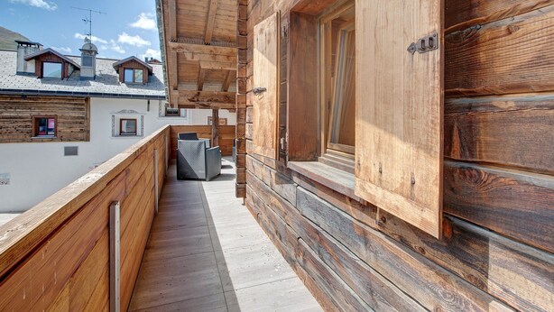 Een houten balkon met een metalen hekwerk, een houten deur en een raam.