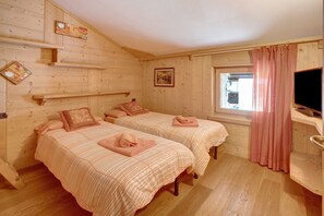 Une chambre dans une cabane en bois, avec deux lits, une fenêtre avec des rideaux, une télévision et des étagères en bois.
