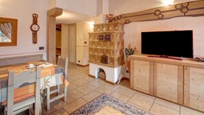 Een houten eettafel met stoelen, een televisie op een houten kast en een decoratieve klok aan de muur.