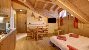 Ein gemütliches Schlafzimmer im Dachgeschoss mit Holzbalkendecke, einem Bett, einem Schreibtisch und einem Fernseher.
