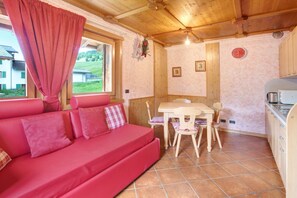 A cozy room with a red sofa, wooden ceiling, a dining table with chairs, and a kitchen area.