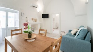 Een moderne woonkamer met een houten eettafel, een blauwe bank en een aan de muur bevestigde televisie.