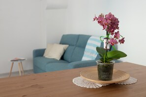 Une orchidée en pot, posée sur une table en bois recouverte d’un chemin de table, un canapé bleu avec un coussin à rayures et un petit tabouret dans un salon.