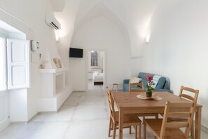 A dining area with a wooden table and chairs, a small side table, and a blue sofa in the background.