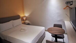 A modern hotel room with a single bed, bedside table, lamp, and a small round table with chairs.