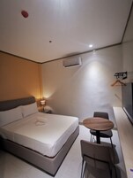 Habitación de hotel moderna con una cama individual, mesita de noche, lámpara y una pequeña mesa redonda con sillas.