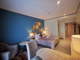 Una habitación de hotel moderna con una cama grande, una mesita de noche con lámpara, una silla y una pequeña mesa redonda.