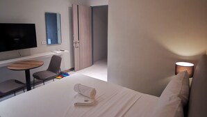 A modern hotel room with a bed, a desk, a chair, a television, and a lamp.