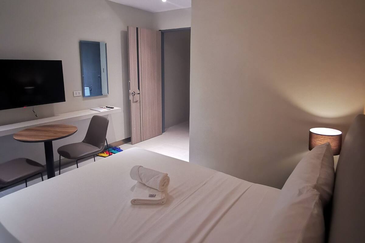 Moderni hotellihuone, jossa on sänky, työpöytä, tuoli, televisio ja lamppu.