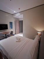 Una habitación de hotel moderna con cama, escritorio, silla, televisor y lámpara.