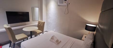 A hotel room with a bed, a TV, a chair, a table, and a lamp.