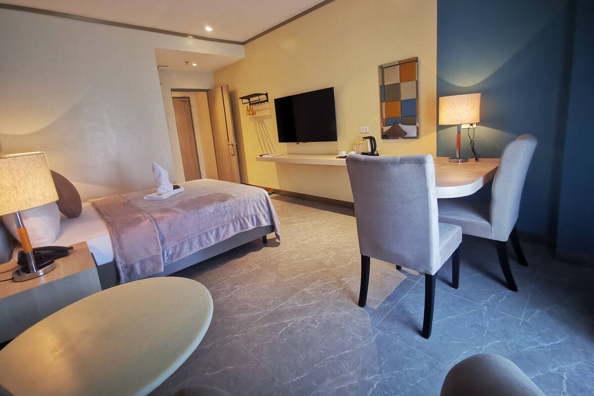 Hotellihuone, jossa on sänky, työpöytä, tuoli, televisio ja lamppu.