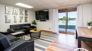Una sala de estar moderna con un sofá de cuero negro, una mesa de centro de madera, un tapete a rayas y un gran ventanal con vistas al lago.