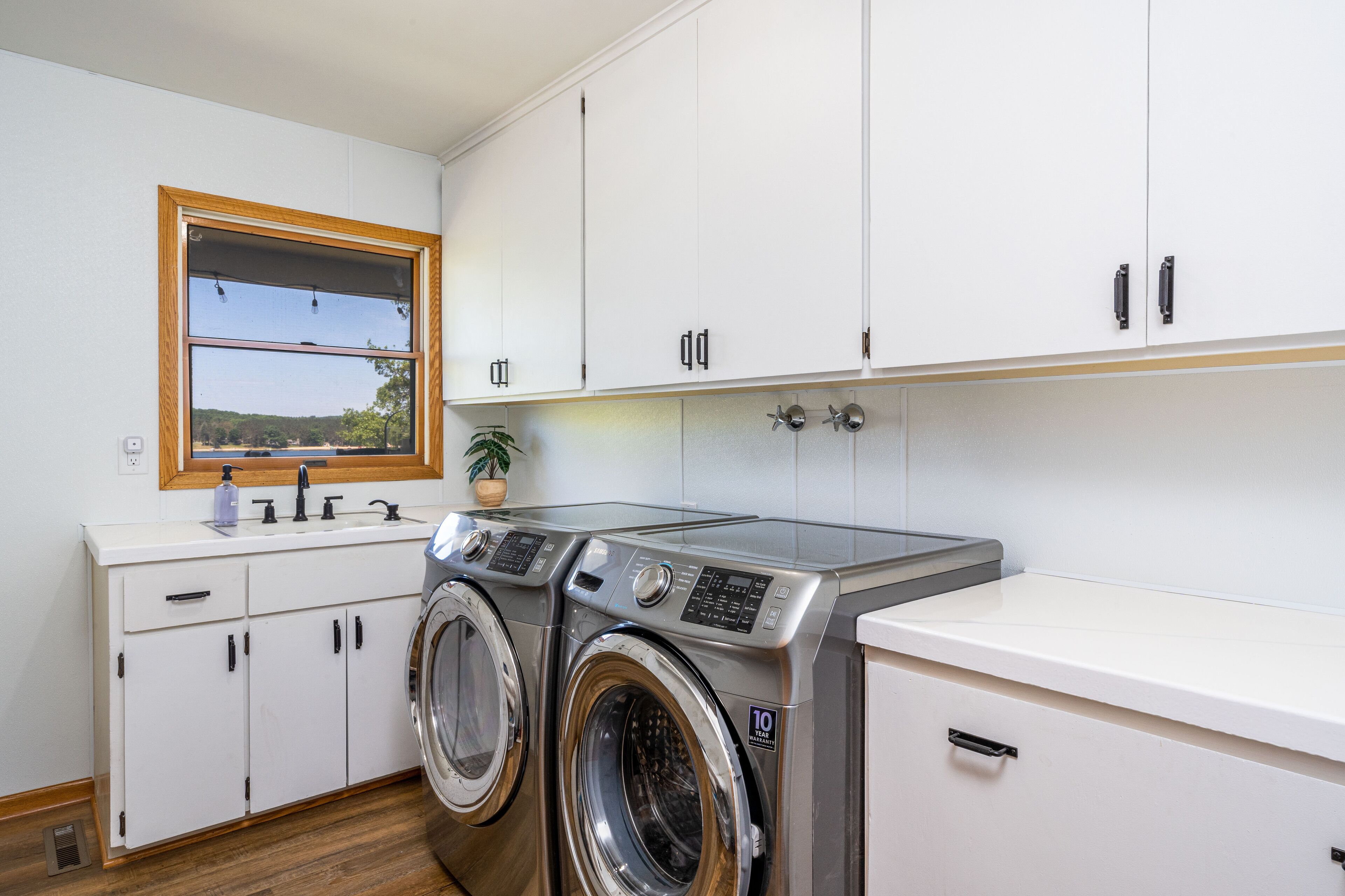 A laundry room with a washing machine, dryer, and a sink with a window above.