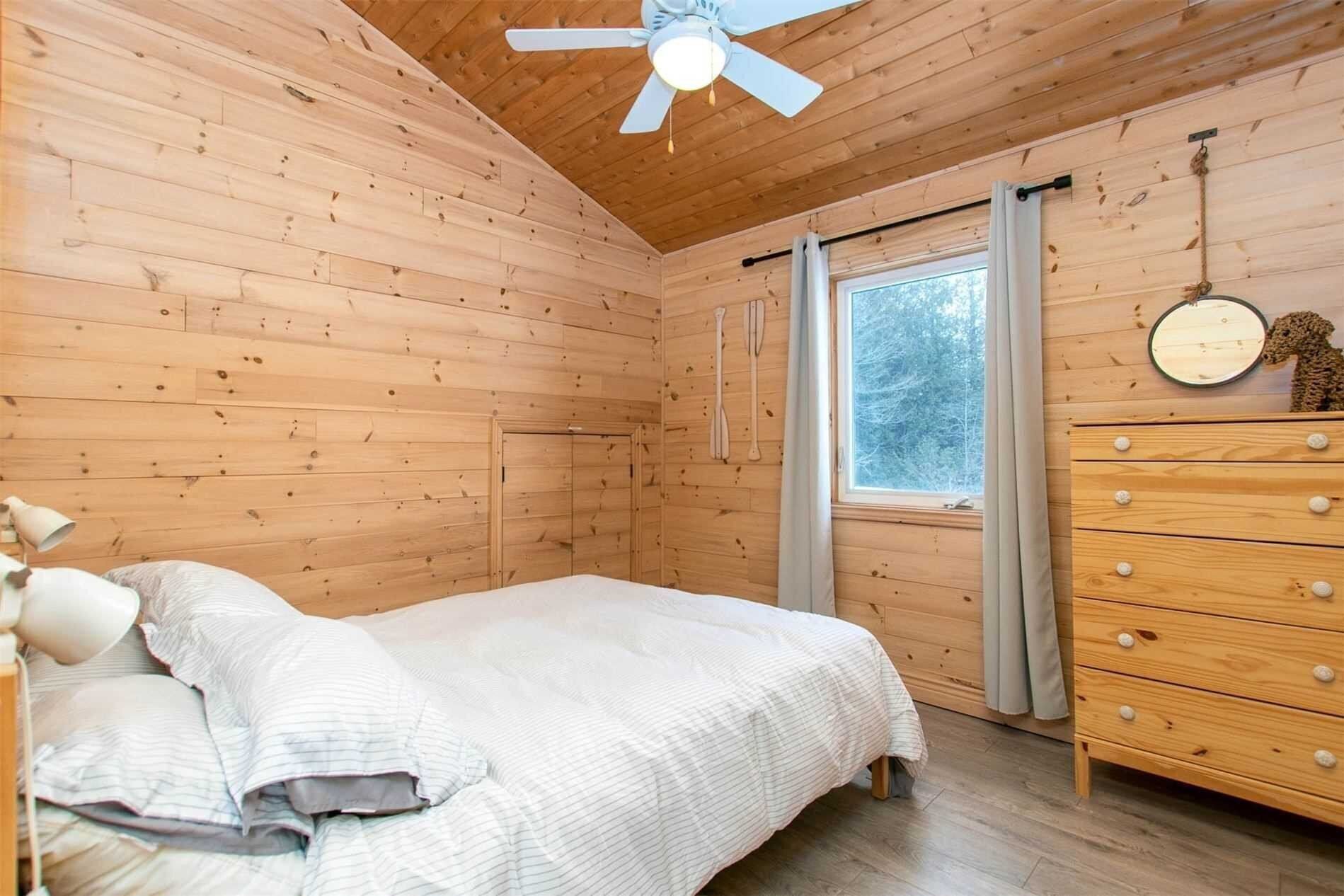 A wooden cabin bedroom with a bed, dresser, and ceiling fan.