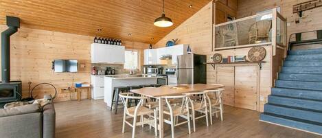 A cozy cabin interior with a wooden interior, a dining area, kitchen, and a staircase.