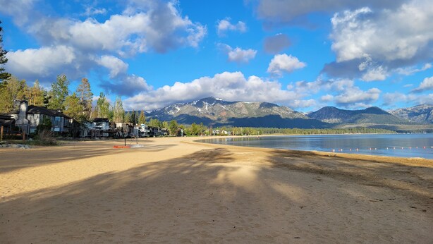A beach with a clear view of mountains in the background, a sandy area, and some buildings near the water.